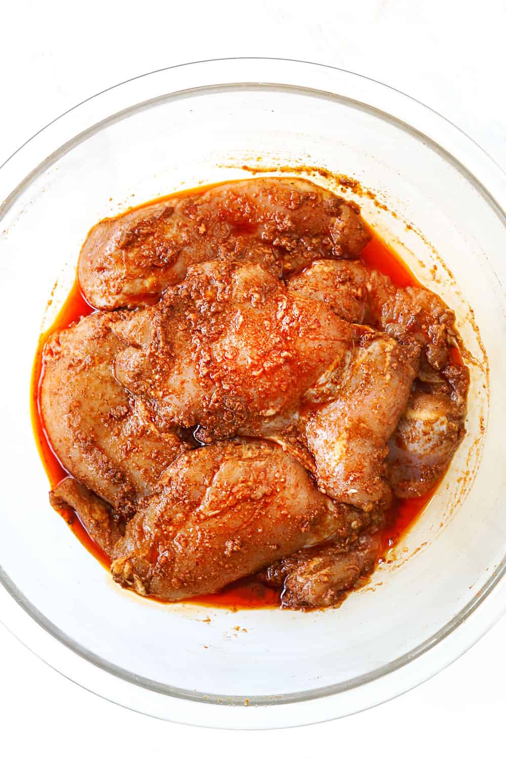 showing how to make harissa chicken by adding chicken to a glass bowl with the mainade