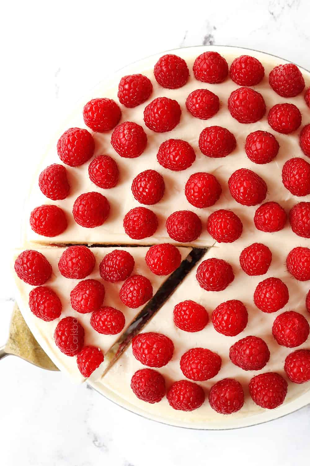 showing how to make white chocolate raspberry cake by covering the top with raspberries