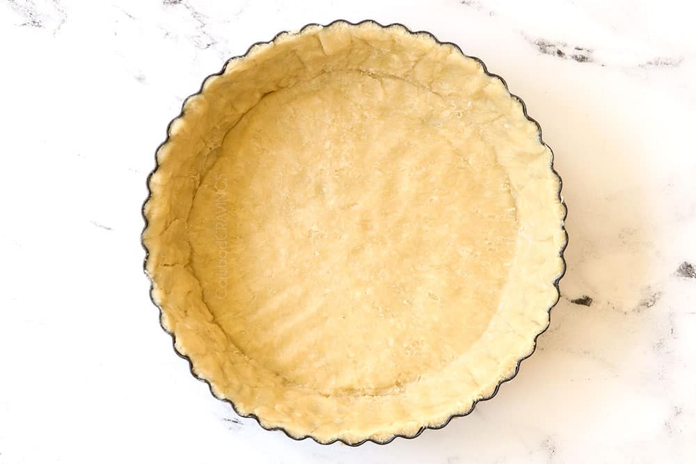 showing how to make pie crust by adding dough to a fluted pan