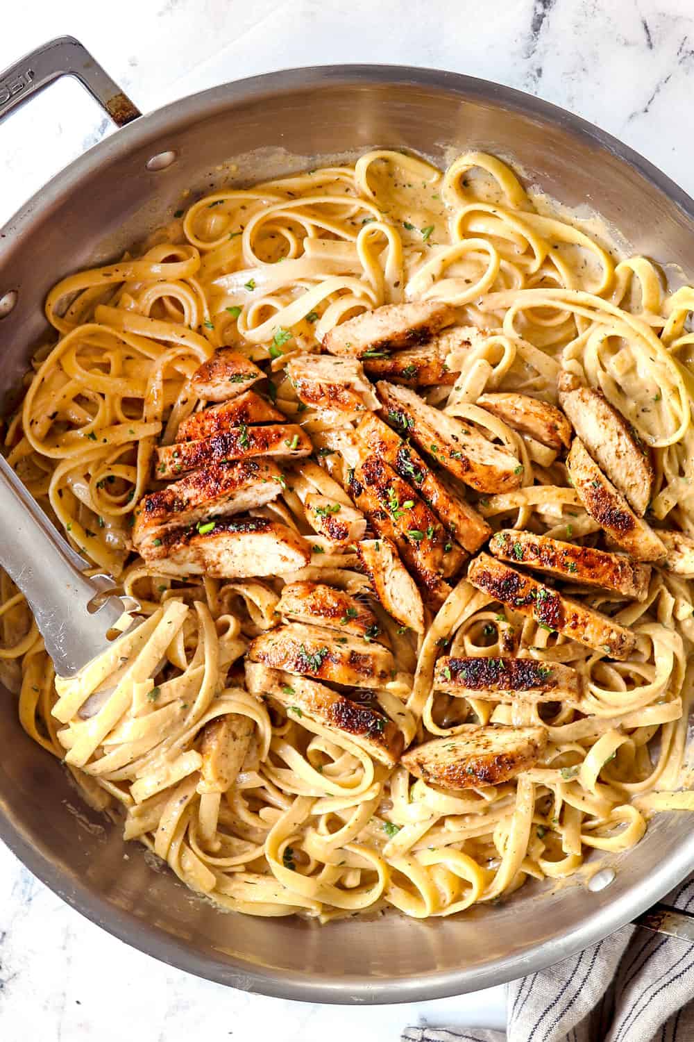 top view of Blackened Chicken Alfredo in a stainless steel skillet with fettucine twisted around tongs 