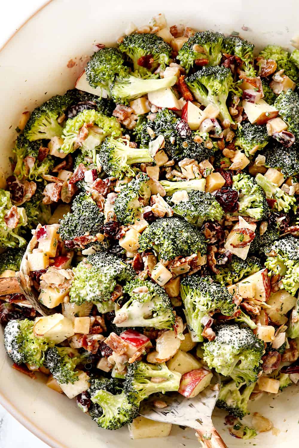 top view showing how to make best broccoli salad by tossing all of the ingredients together in a white bowl