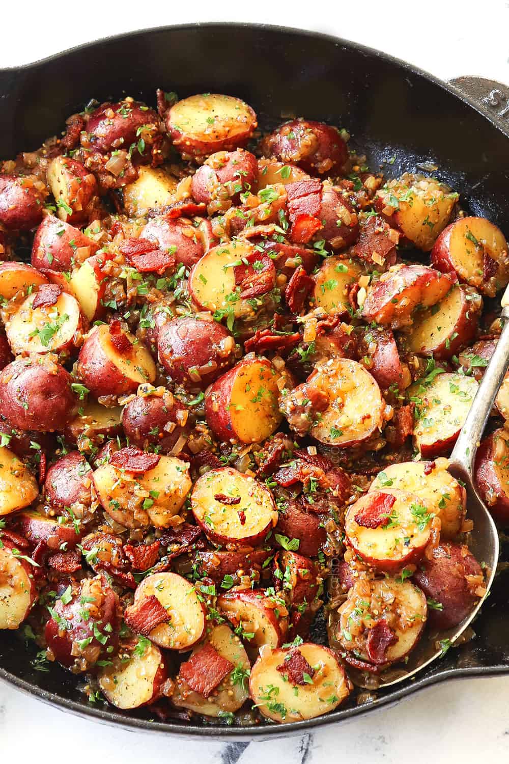 showing how to make German potato salad by tossing the potatoes with the dressing and bacon in a skillet