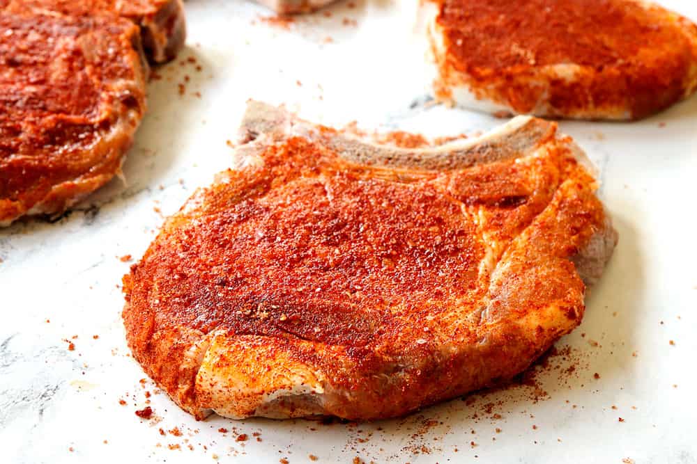 showing how to make grilled pork chops by seasoning them with a spice rub