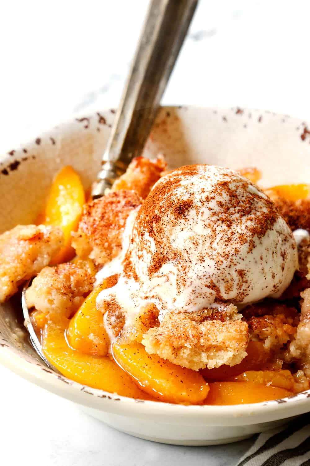 showing how to serve easy peach cobbler recipe by adding a scoop of vanilla ice cream