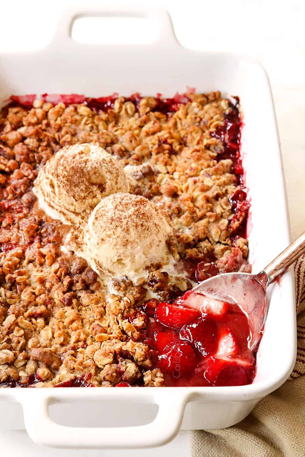 strawberry crisp recipe (or crumble) baked in a white dish with a serving spoon scooping up the strawberry dessert