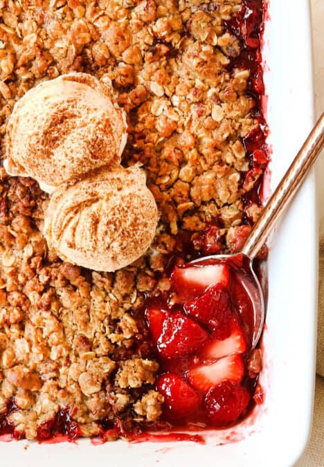 top view of strawberry crisp recipe topped with vanilla ice cream with a serving spoon
