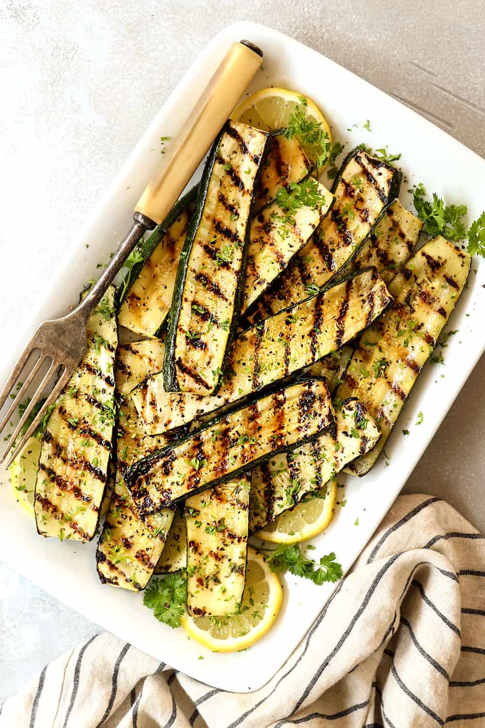 showing how to grill zucchini by adding it to a serving platter and sprinkling with fresh herbs