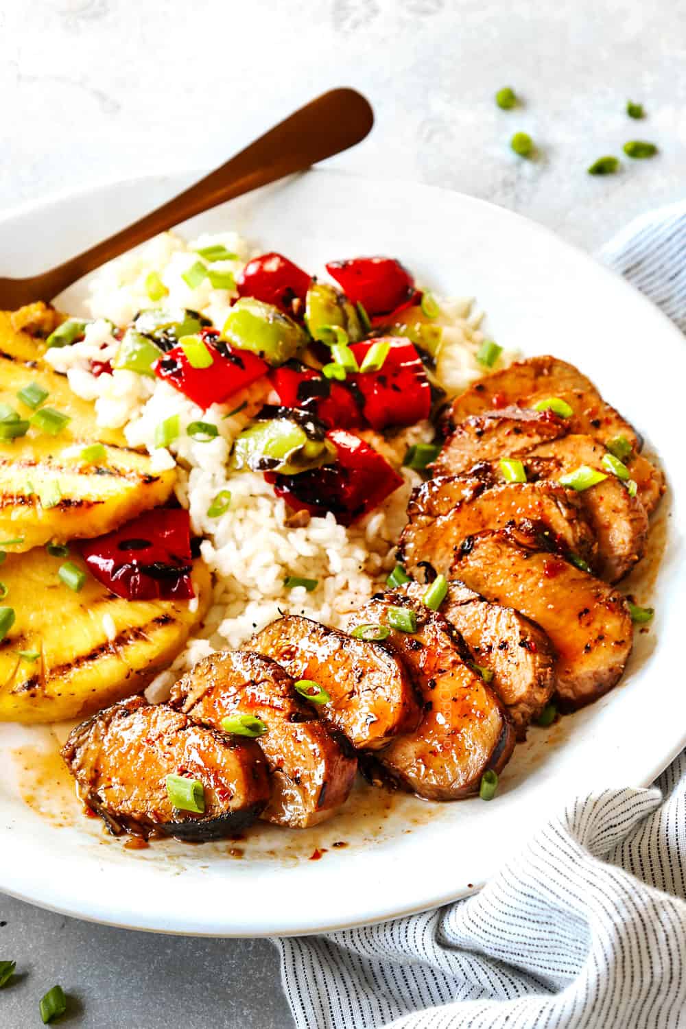 sliced marinated pork tenderloin on a white plate served with rice and grilled vegetables