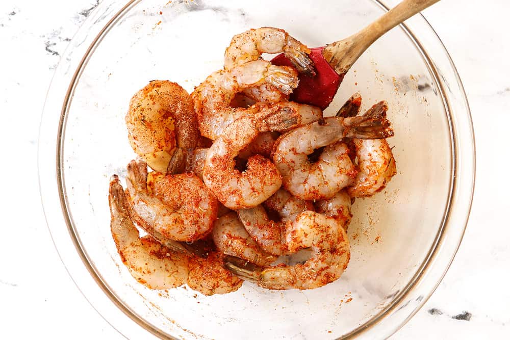 showing how to make Cajun shrimp by mixing shrimp with Cajun seasoning