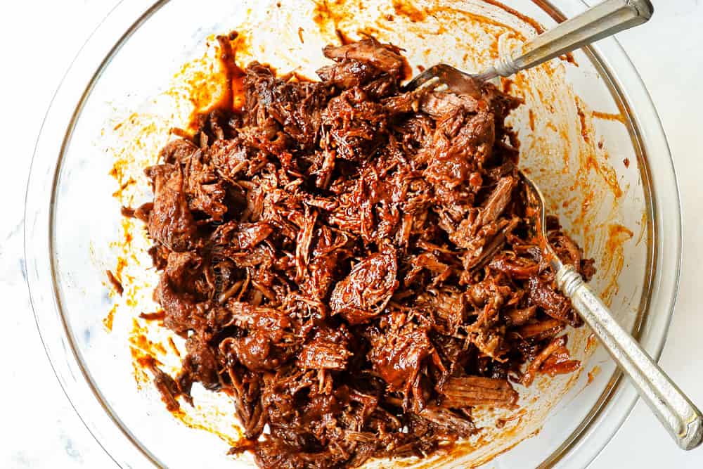 showing how to make birria tacos with birria de res by shredding beef with two forks