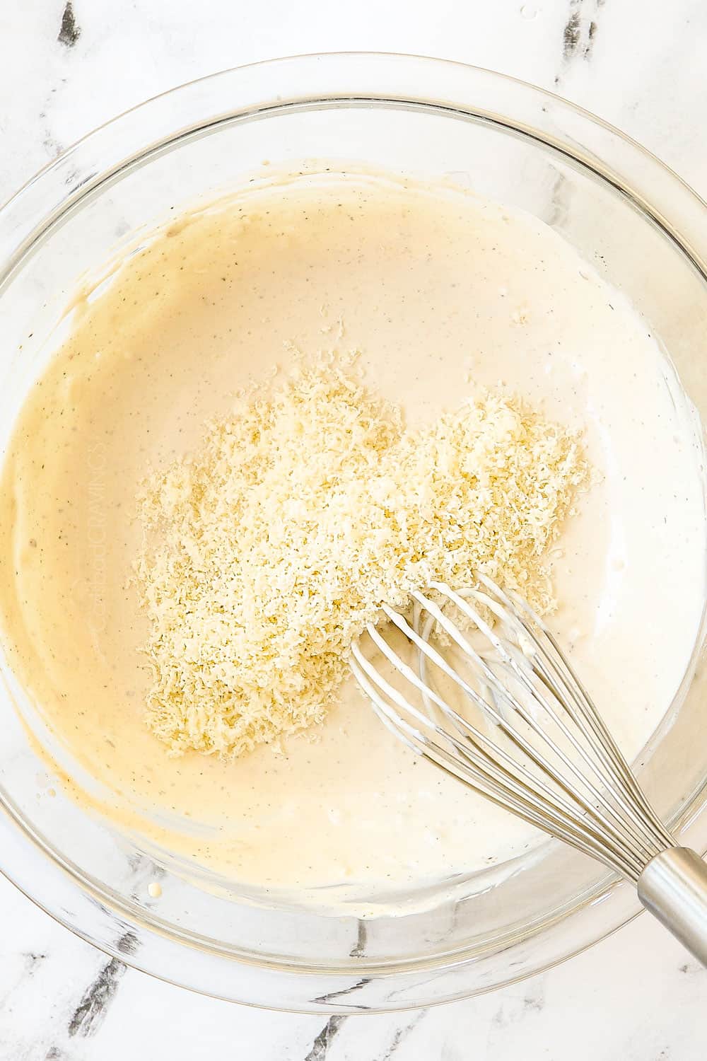 showing how to make Caesar Dressing by whisking finely grated Parmesan into a bowl with the dressing