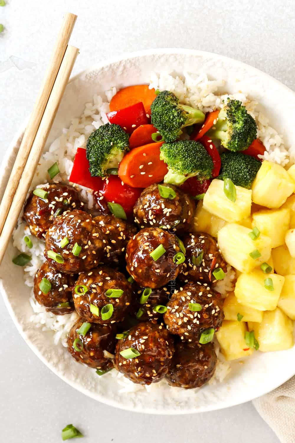 showing how to serve teriyaki meatballs by adding to a plate with pineapple and stir fried vegetables