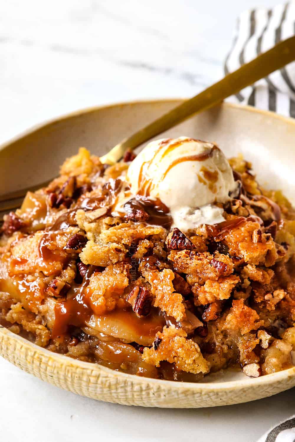 up close of apple dump cake with ice cream and caramel in a bowl