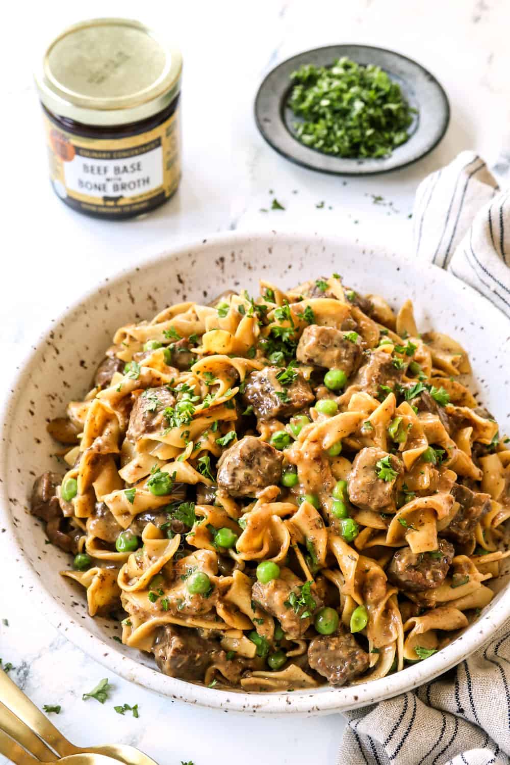 beef tips and noodles in a bowl with peas and fresh parsley