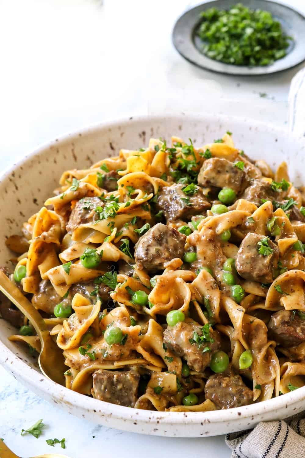 beef tips and noodles in a bowl with peas and fresh parsley