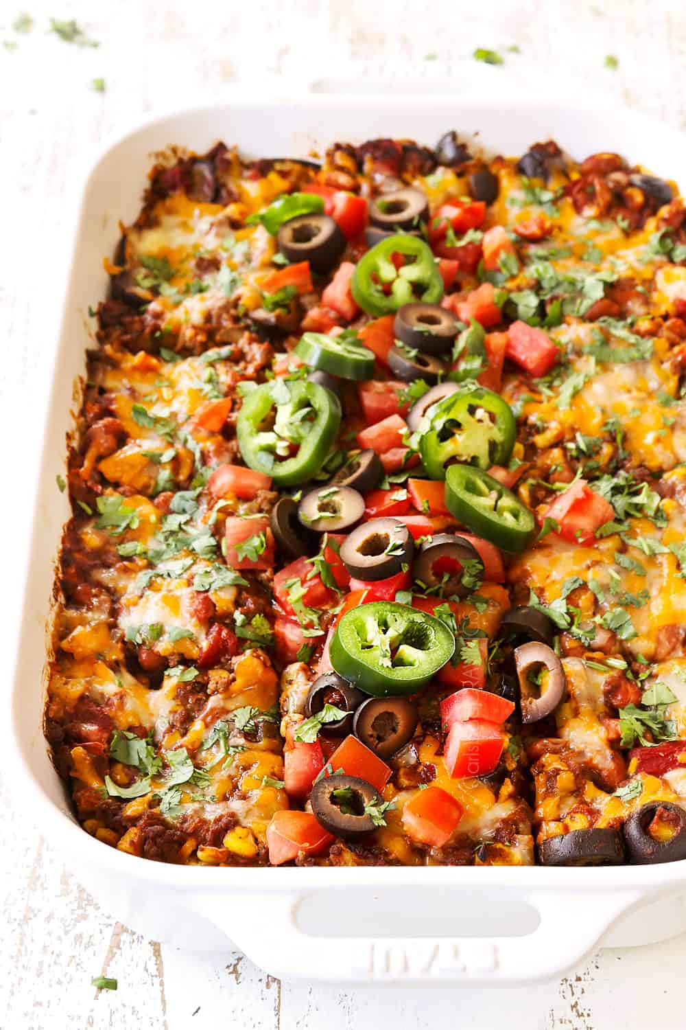 up close of enchilada casserole recipe sliced into slices garnished with tomatoes, olives and jalapenos