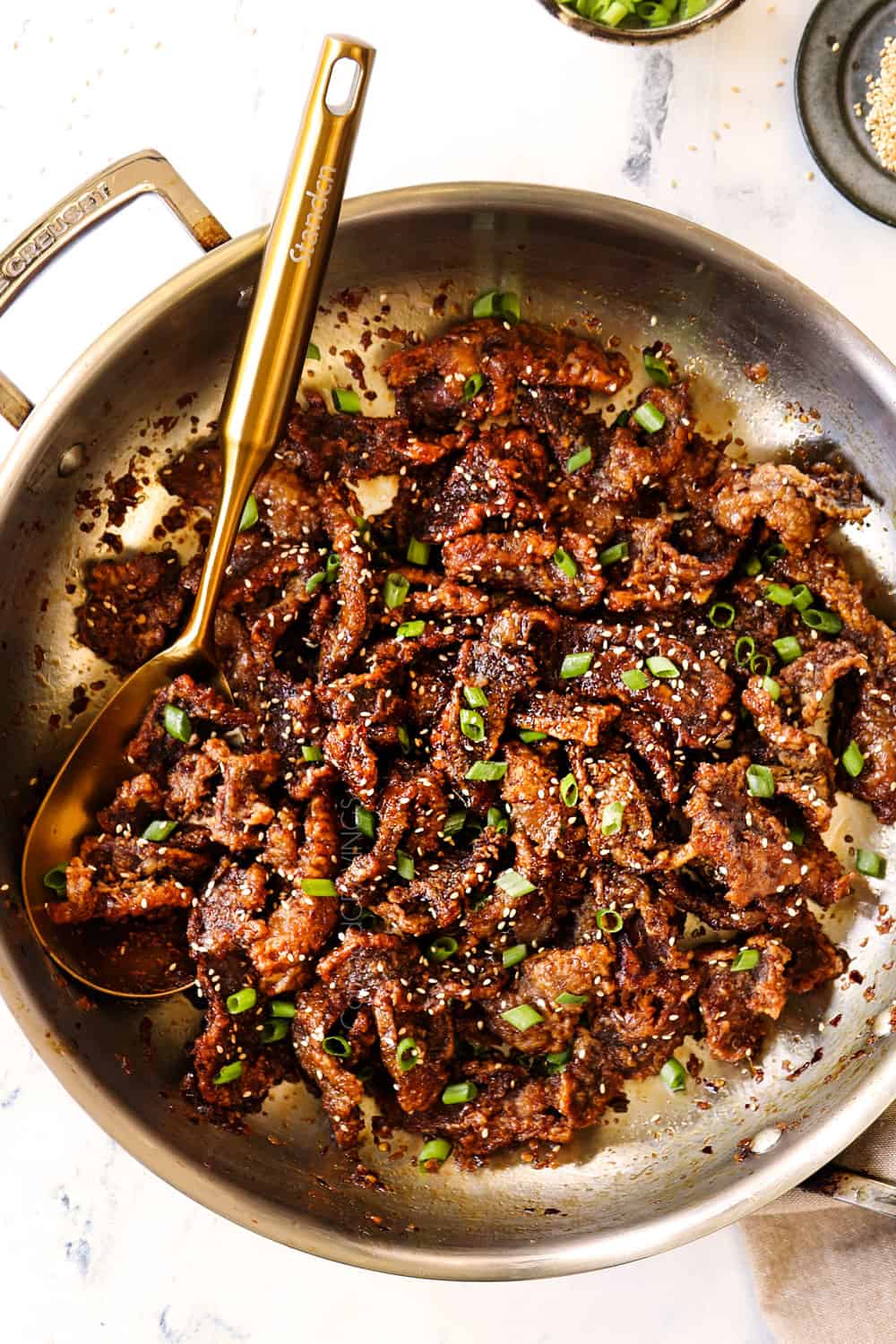 showing how to make Ginger Beef recipe by tossing the fried beef in the sauce