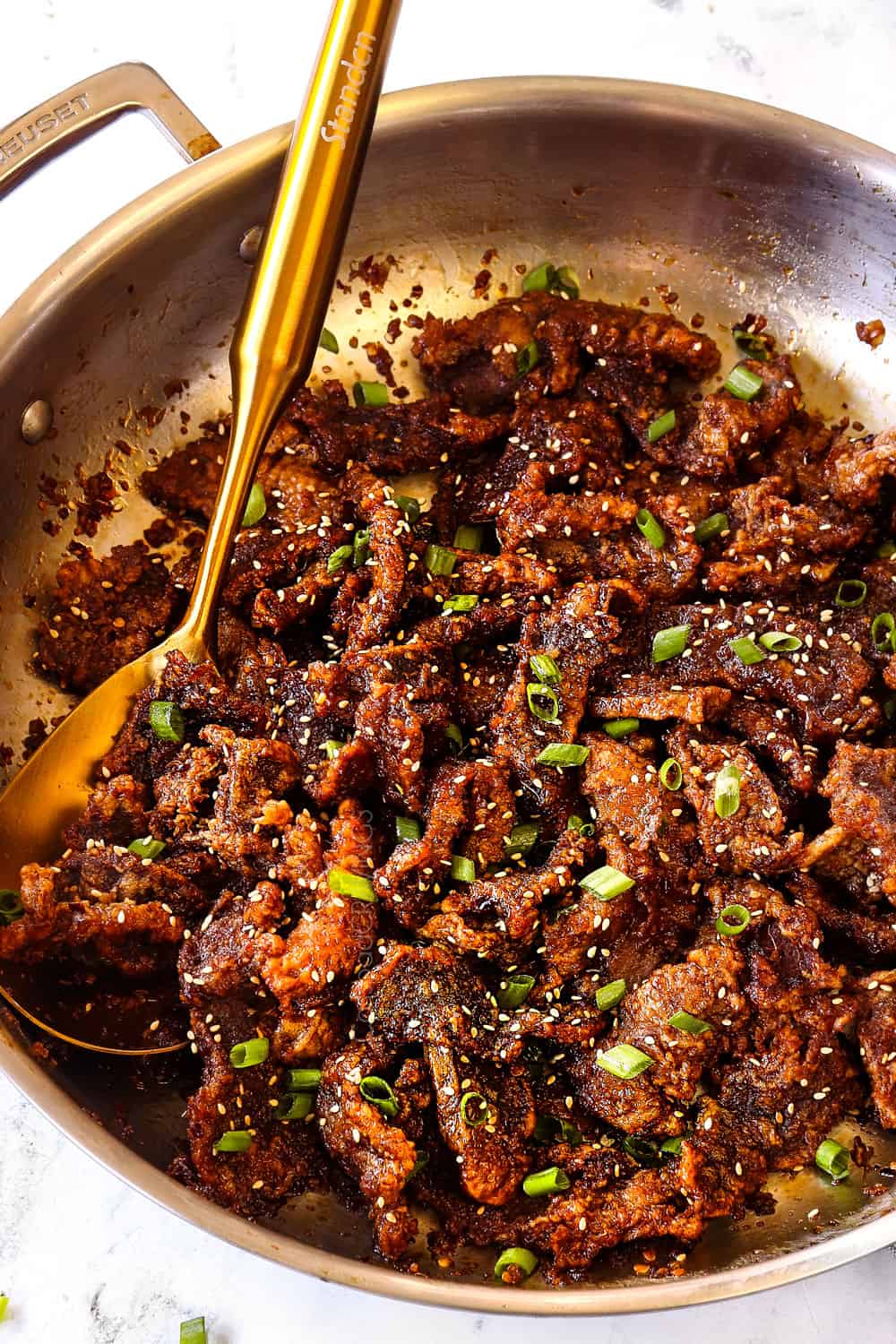 showing how to make ginger beef by garnishing with sesame seeds and green onions
