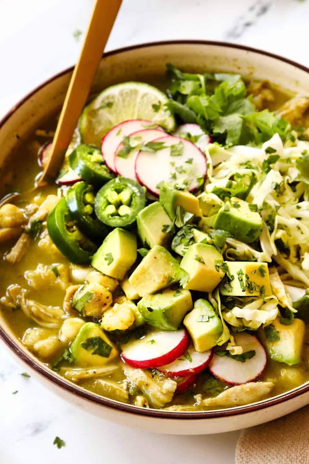 up close of chicken pozole verde (posole) in a bowl with chopped avocados, cilantro, radishes