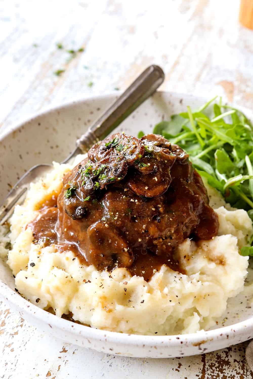 showing how to serve homemade Salisbury Steak by adding to a plate with mashed potatoes