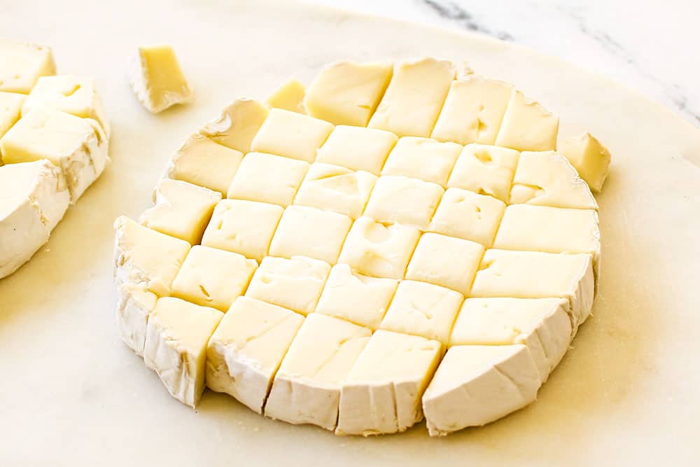 showing how to make cranberry brie bites by cutting brie cheese into cubes