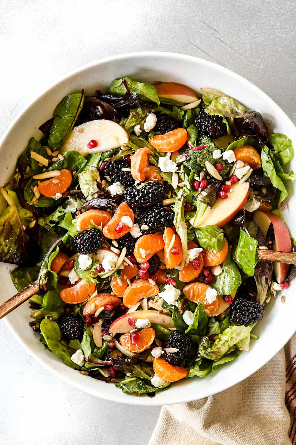 showing how to make Mandarin Orange Salad by tossing mandarins, apples, goat cheese, blackberries and pomegranates together with dressing