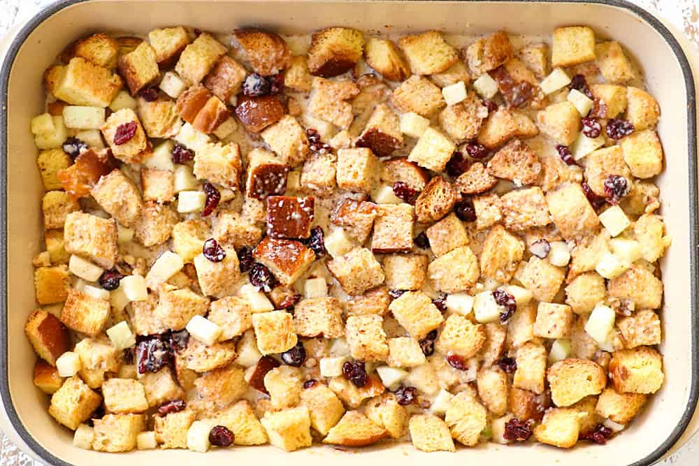 showing how to make apple bread pudding by adding custard to cubed stale bread in a 9x13 baking dish