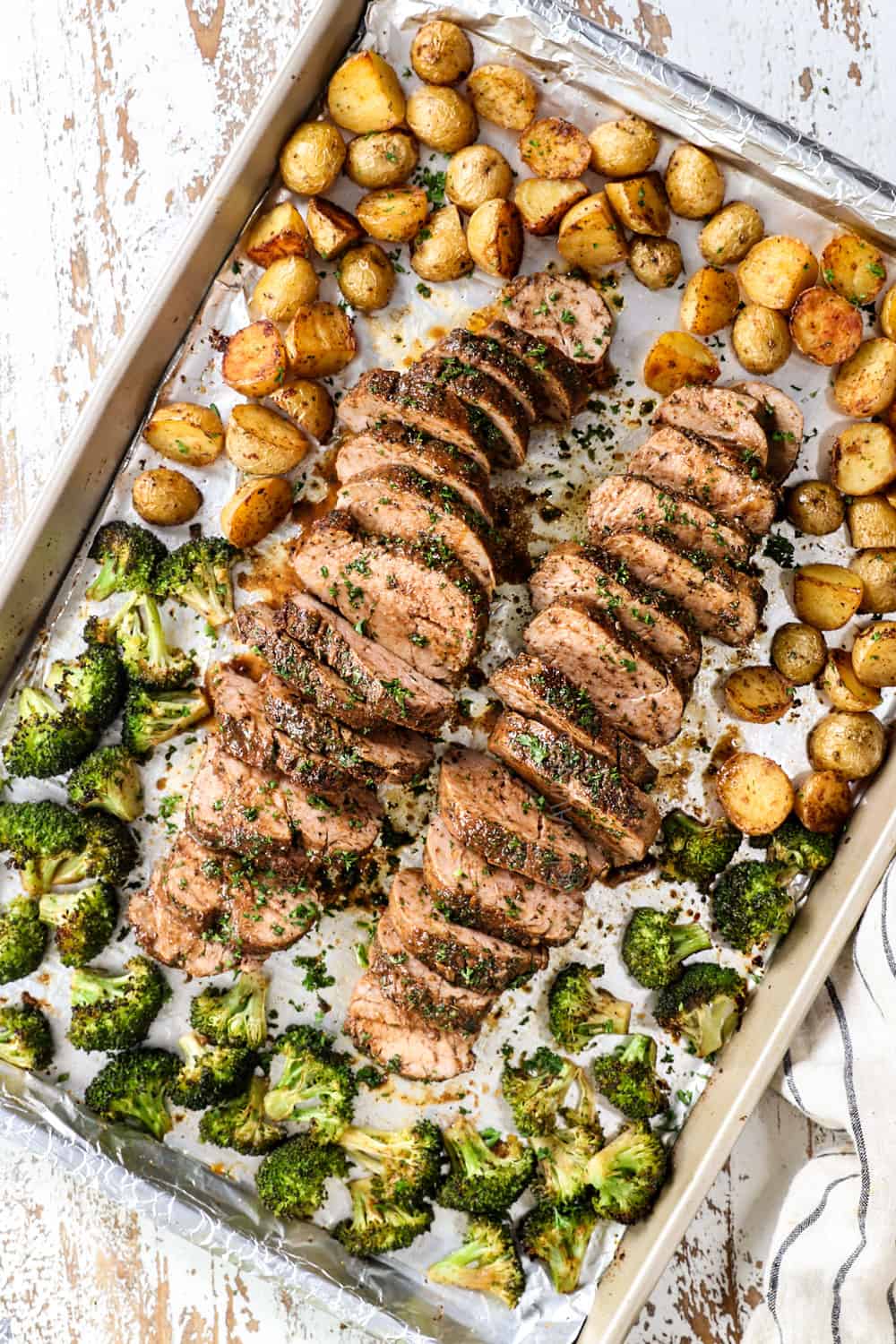 top view of balsamic roasted pork tenderloin sliced on a baking sheet oven roasted with potatoes and broccoli