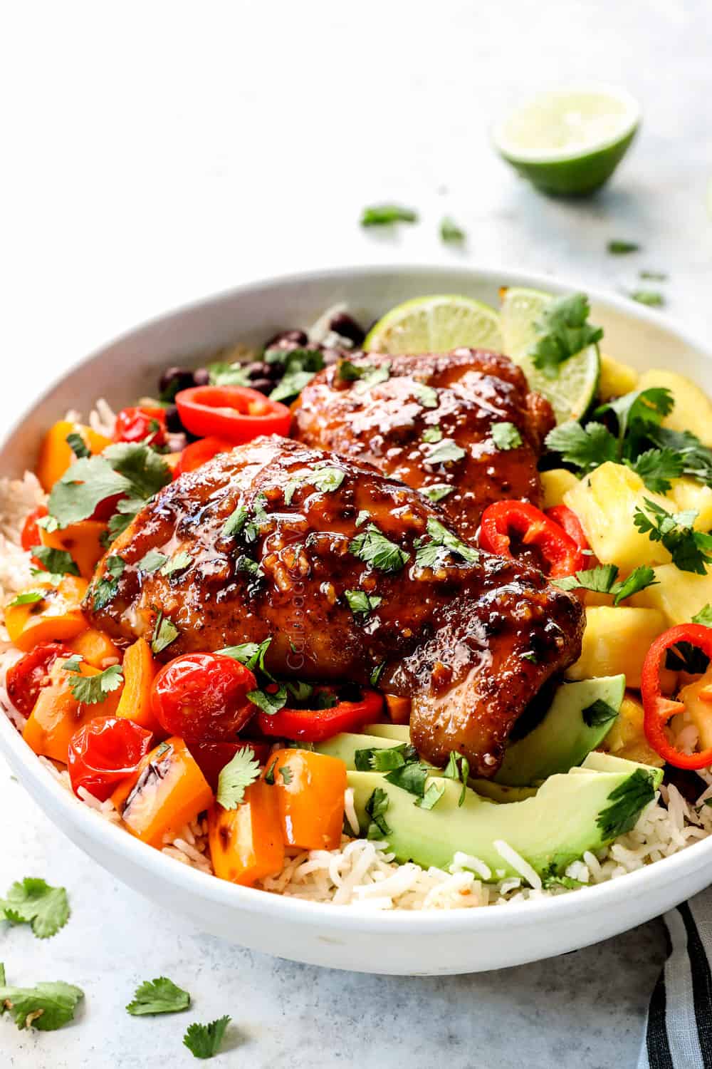showing how to serve honey lime chicken by adding thighs to a bowl with rice, pineapple, avocados and cilantro