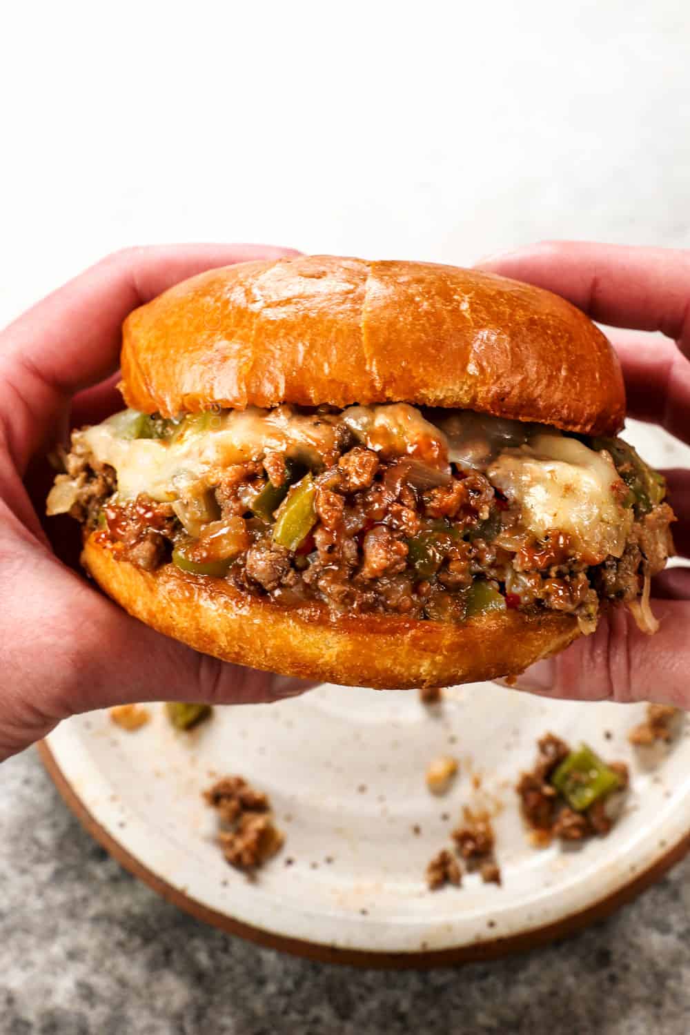 a hand holding a Philly Cheesesteak Sloppy Joe showing the melty cheese and saucy filling