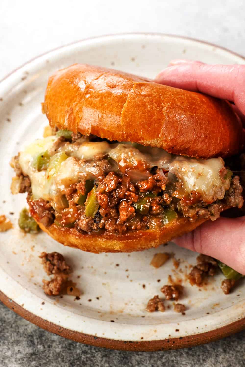 a hand holding Philly Cheesesteak Sloppy Joe showing the melted cheese and saucy filling
