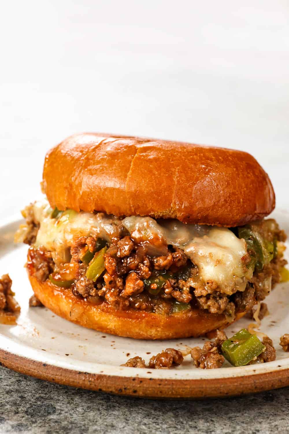 a Philly Cheesesteak Sloppy Joe sitting on a plate with meat spilling out the sides