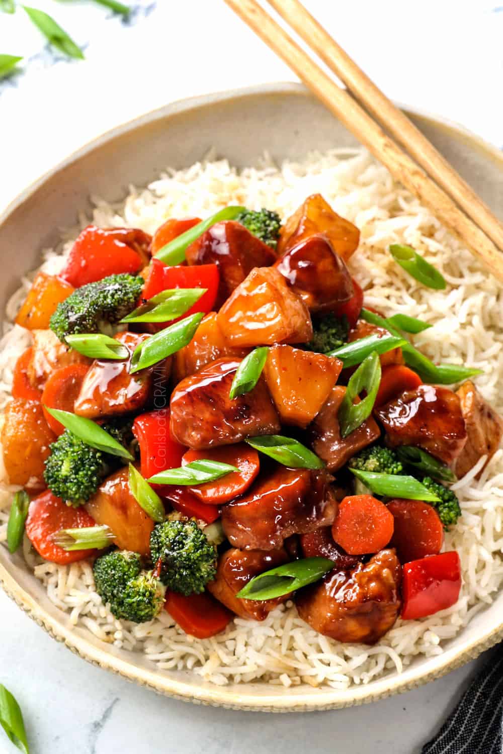 showing how to serve teriyaki chicken stir fry by adding to a bowl of rice with chopsticks
