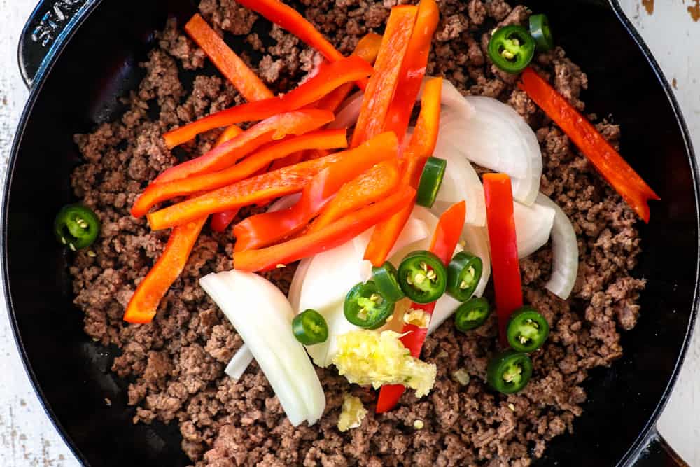showing how to make Thai Basil Beef (pad krapow) by adding onions, chili peppers, garlic and red bell peppers to the ground beef
