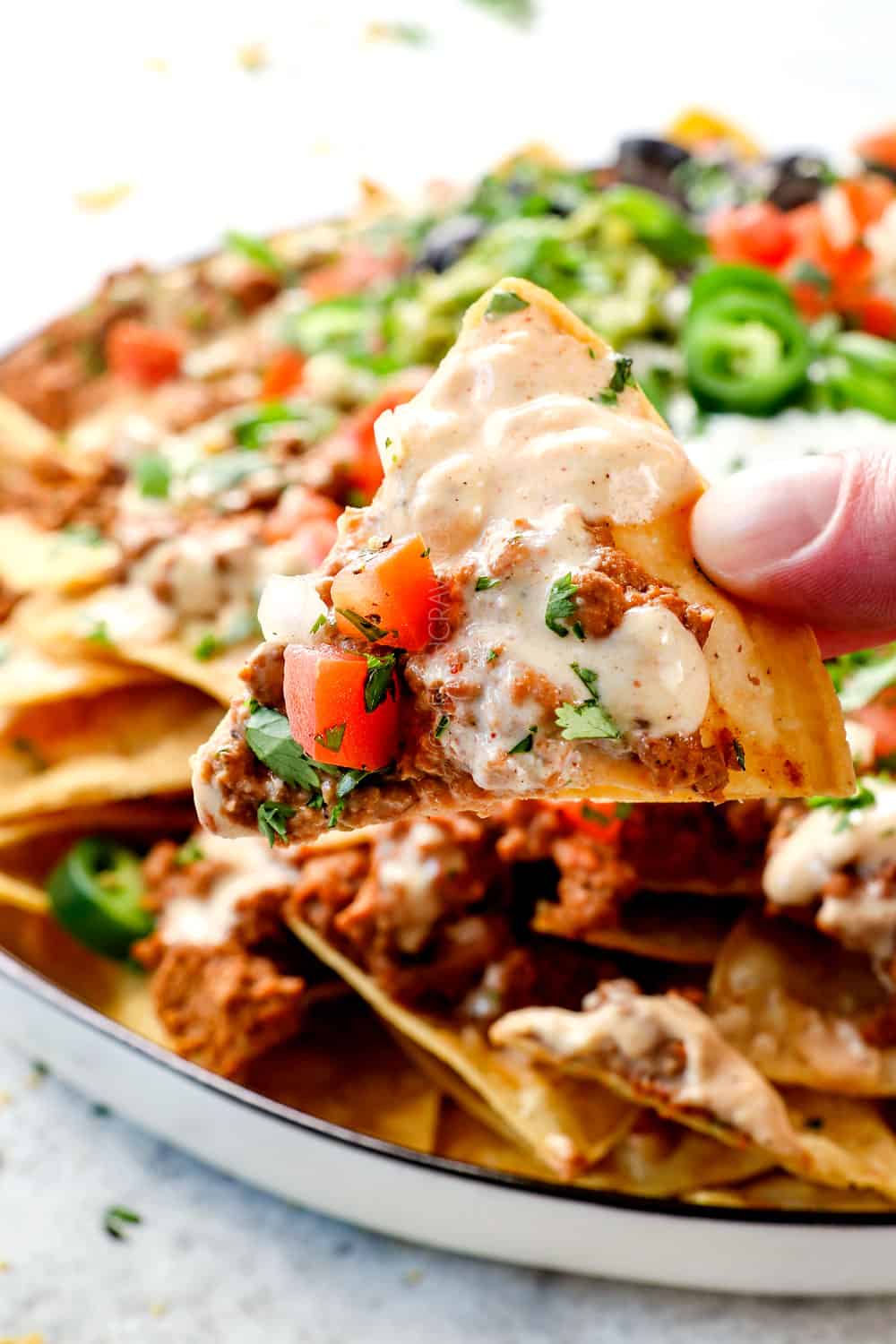 a hand picking up loaded nacho recipe with ground beef, cheese sauce and pico de gallo on the chip