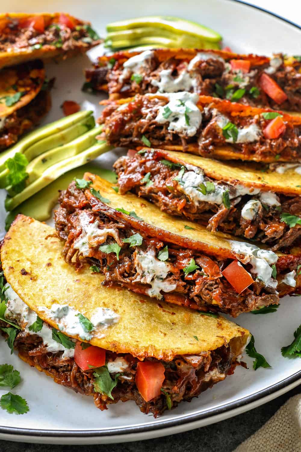 showing how to serve shredded beef tacos by topping with cilantro lime ranch and pic de gallo