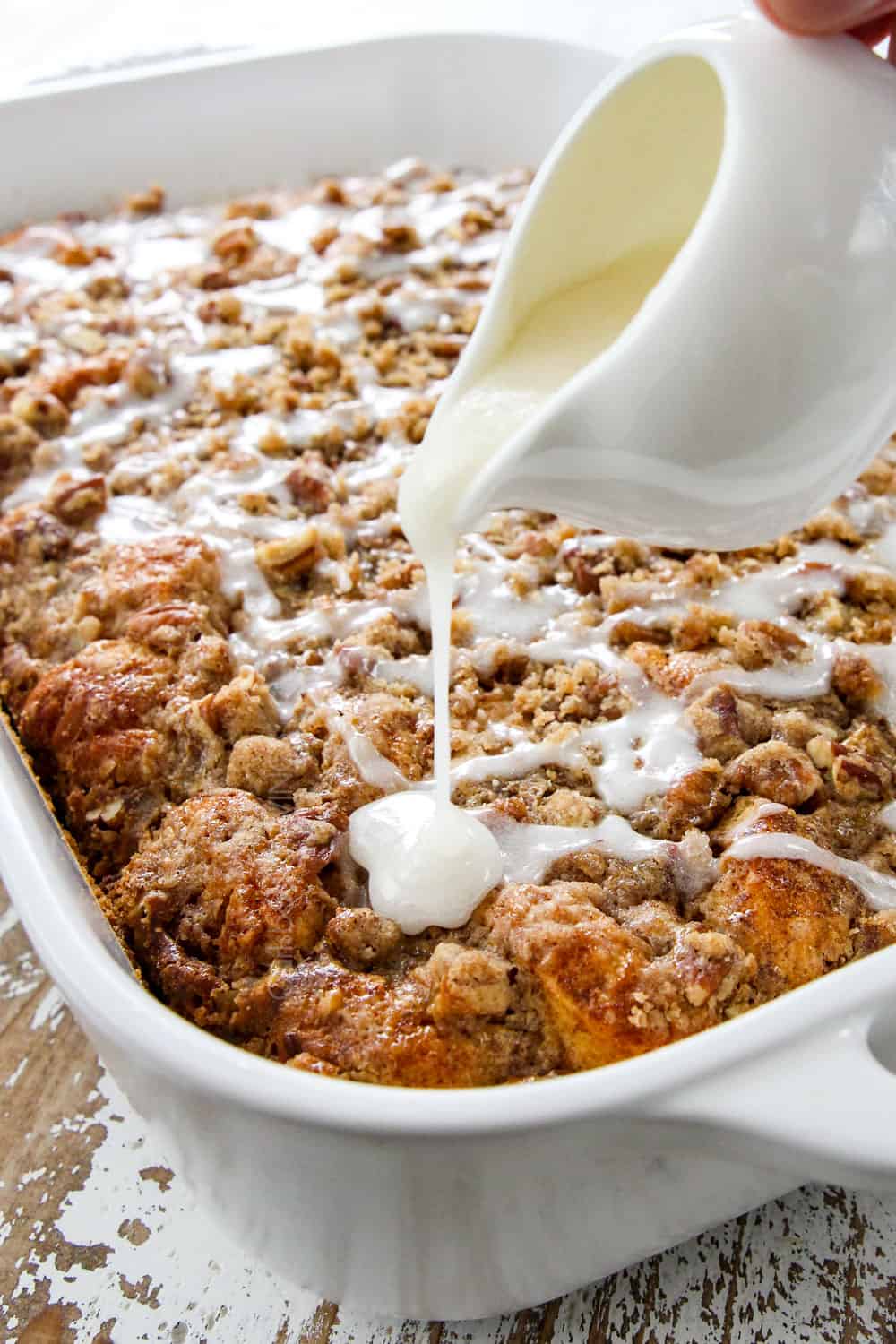 showing how to make Cinnamon Roll French Toast Casserole by drizzling icing over the casserole 