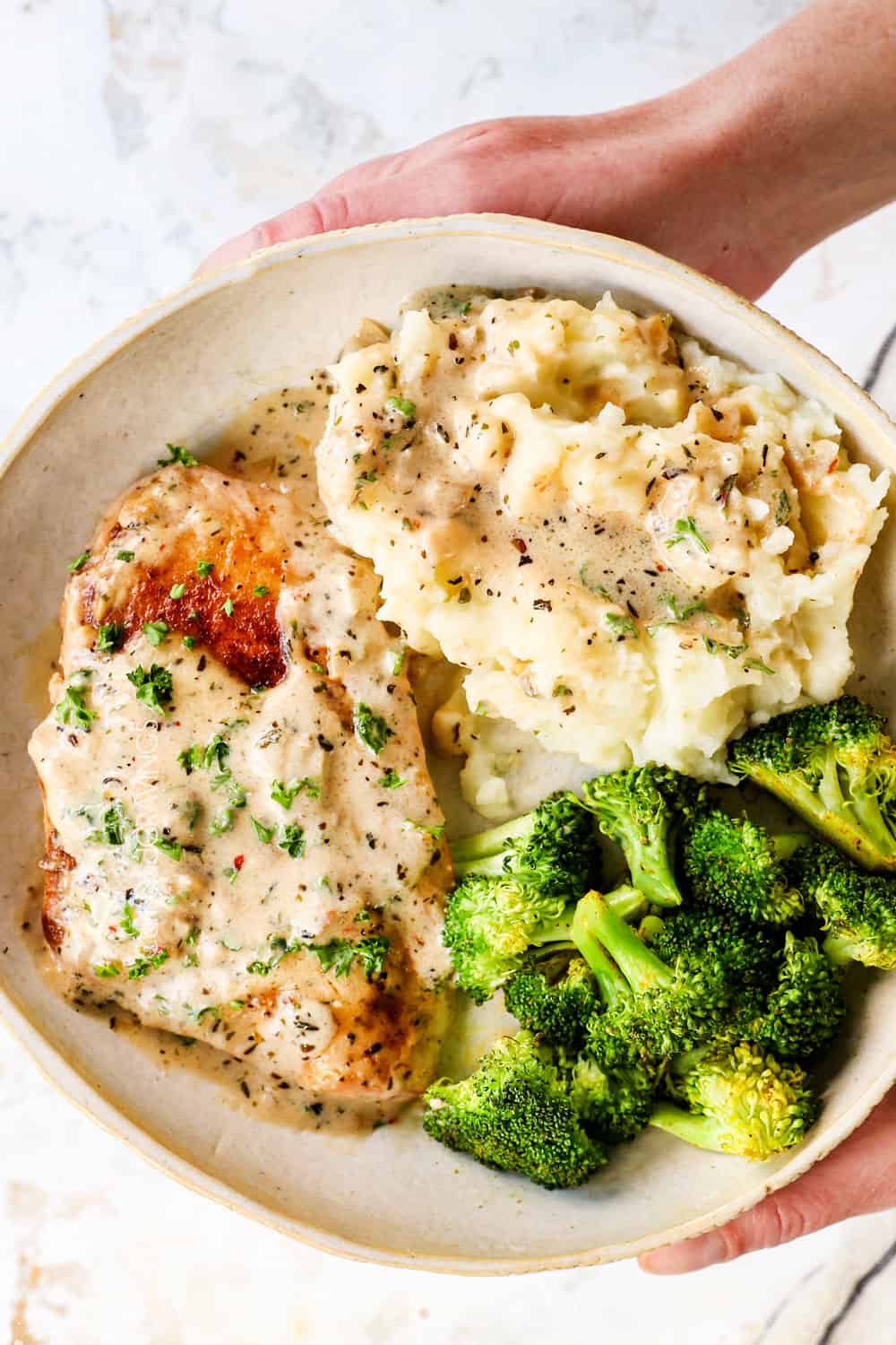 showing how to serve creamy garlic Parmesan chicken by adding to a plate with mashed potatoes and broccoli