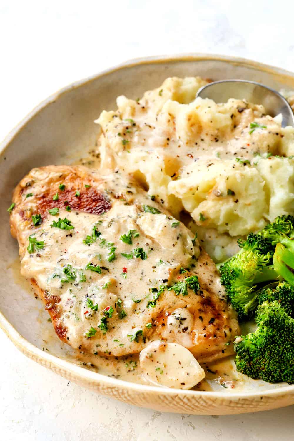 up close view of a piece of creamy garlic chicken with Parmesan sauce over top with mashed potatoes and broccoli on the side