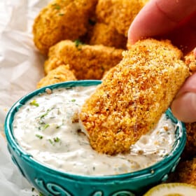 showing how to serve fish sticks by dipping a fish stick in tartar sauce
