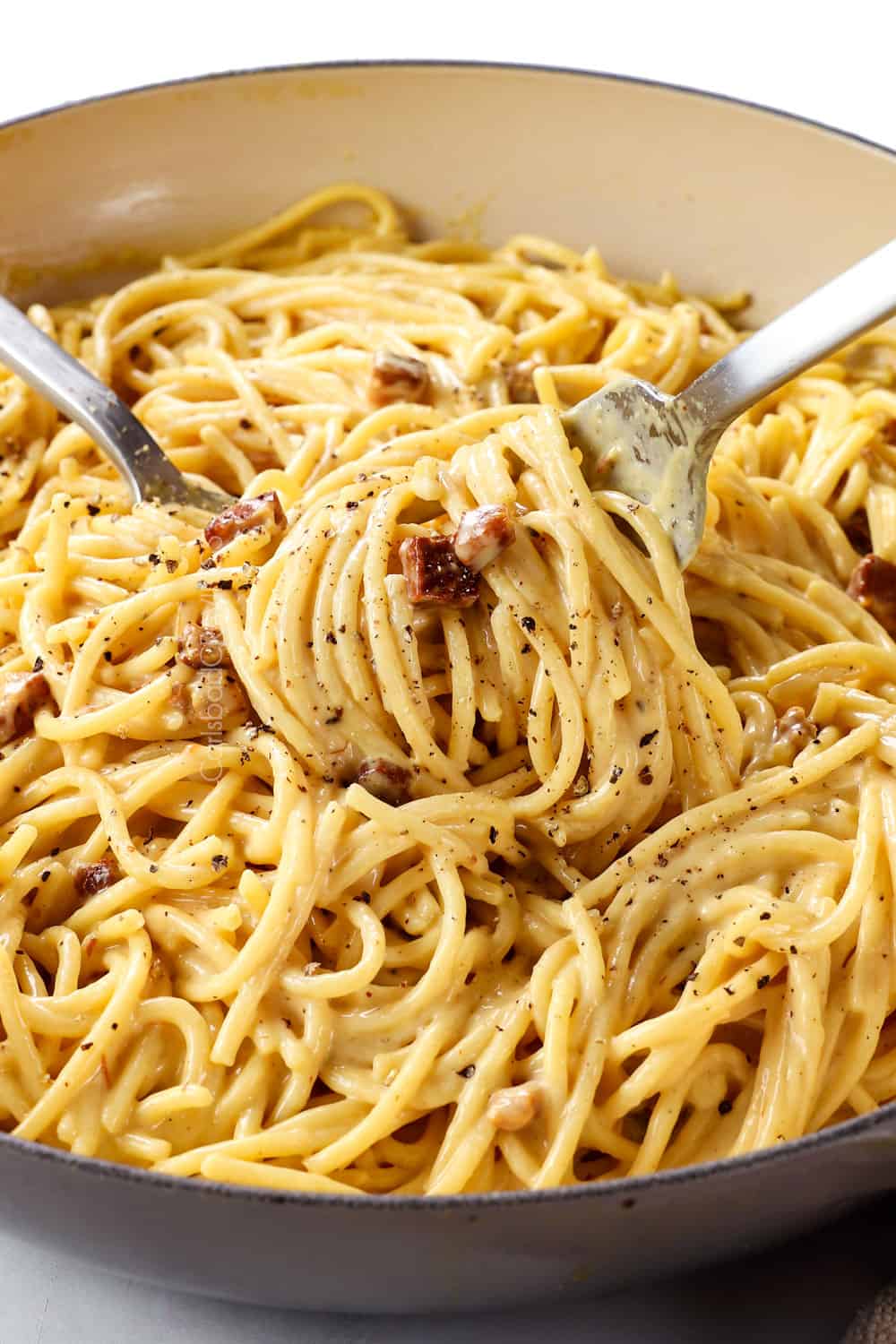up close of tossing spaghetti carbonara with two forks showing how creamy it is