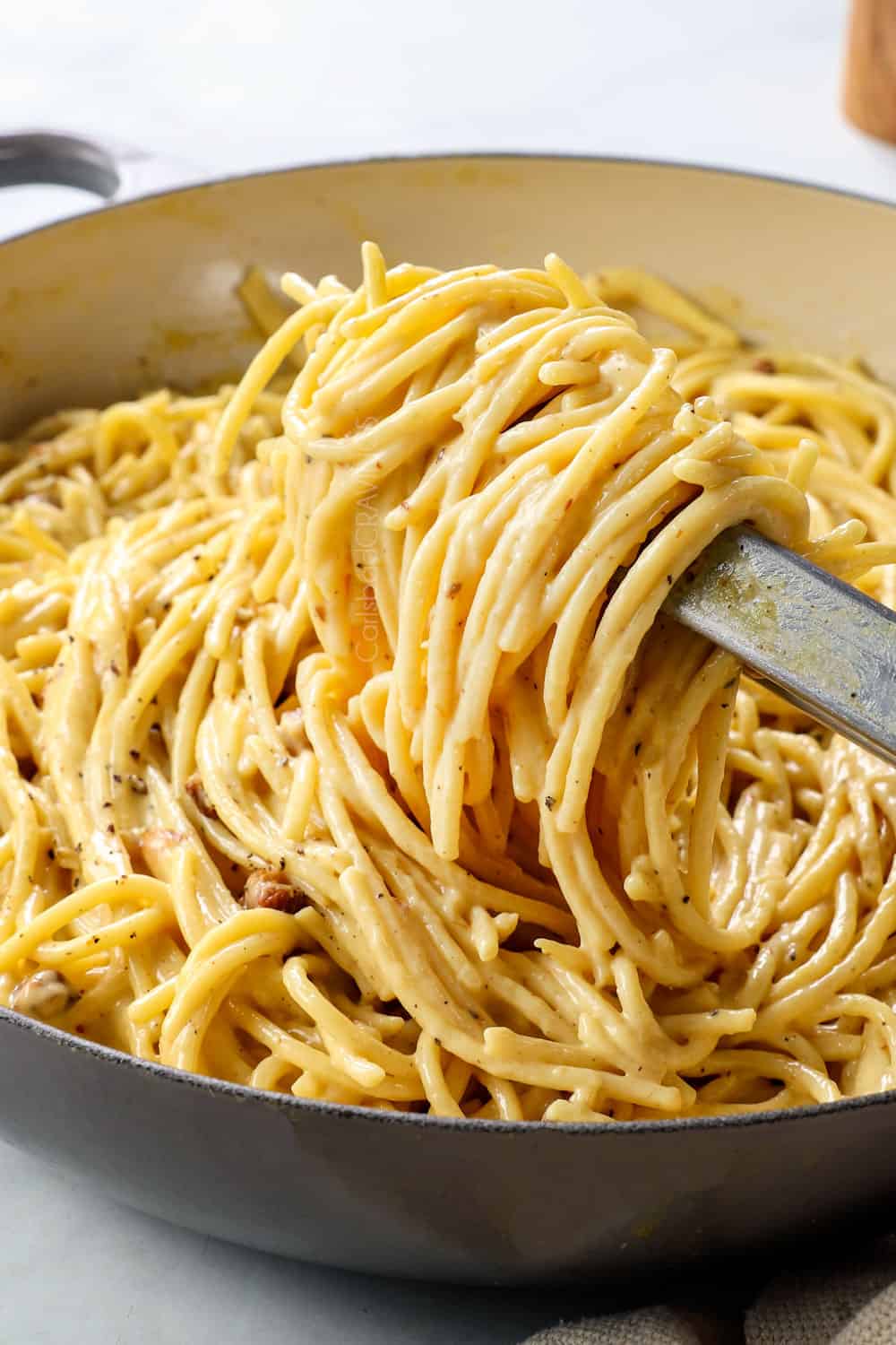 showing how to make carbonara recipe by tossing pasta with egg sauce showing how creamy it is