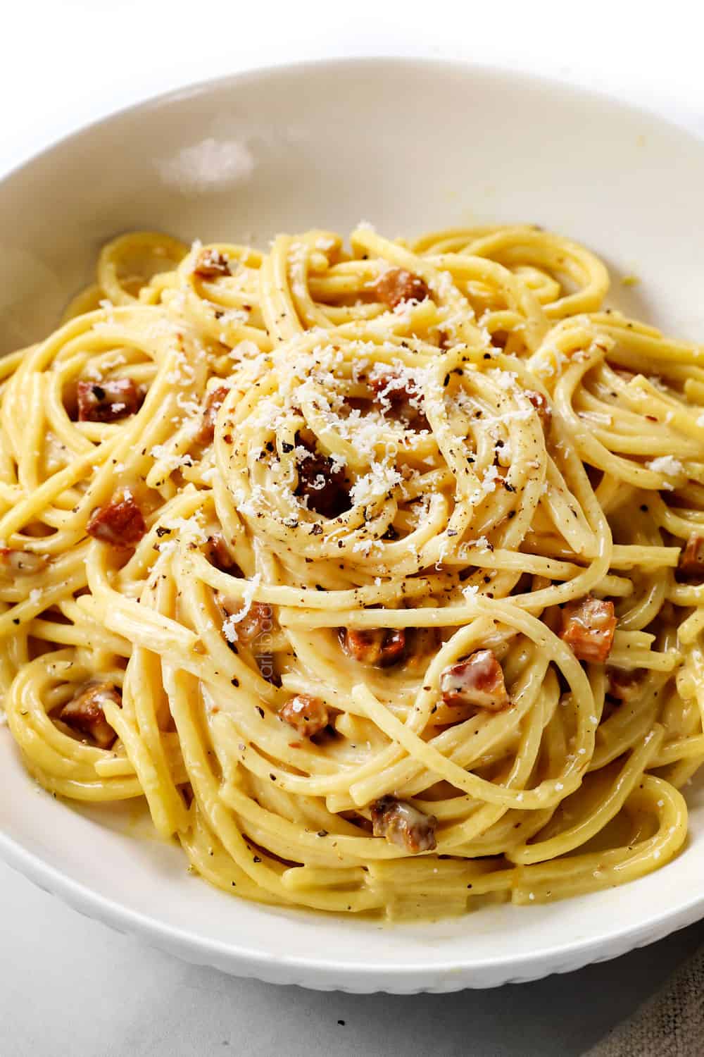 up close of a bowl of spaghetti carbonara showing how to serve garnished with Pecorino Romano and pepper