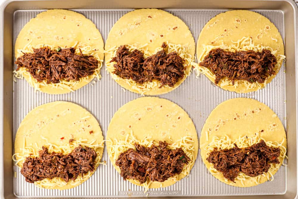 showing how to make beef taco recipe by lining cheese then shredded beef on top of corn tortillas on a baking sheet