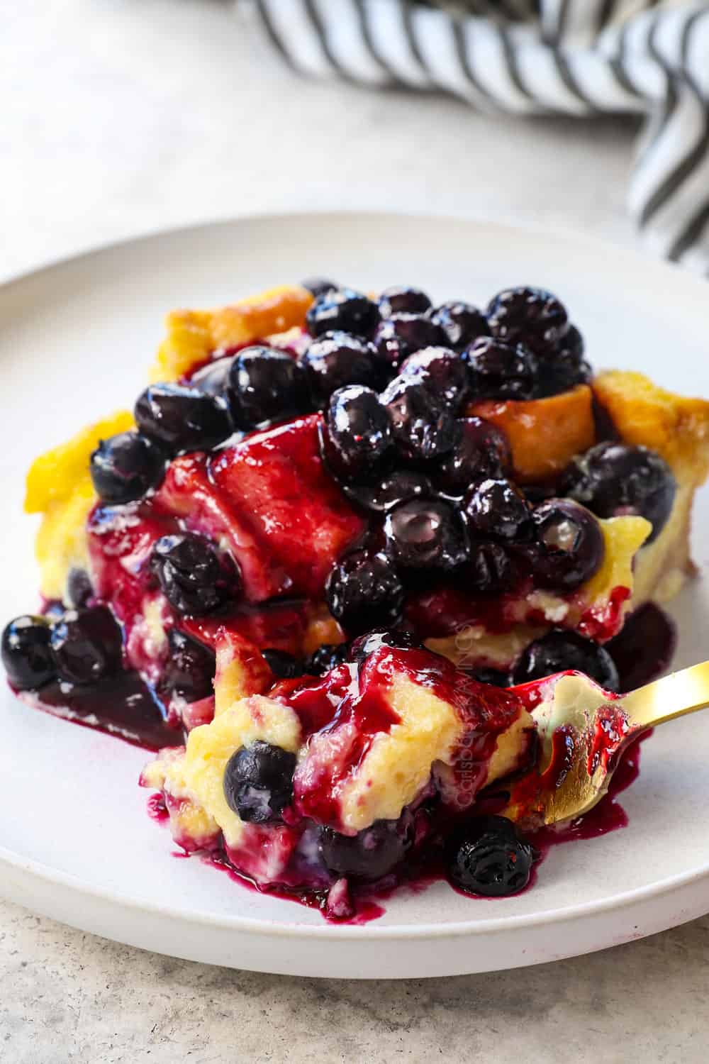 up close of a slice of Blueberry French Toast Casserole with a fork taking a bite showing how creamy the custard is