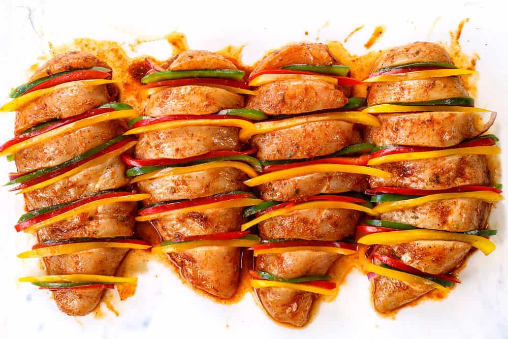 showing how to make Hasselback Chicken by stuffing the slits with slices of red onion and green, yellow and red bell peppers