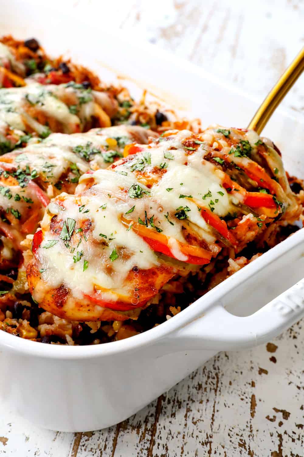 a spatula scooping up Hasselback chicken with fajita bell peppers baked in a casserole dish showing how juicy it is