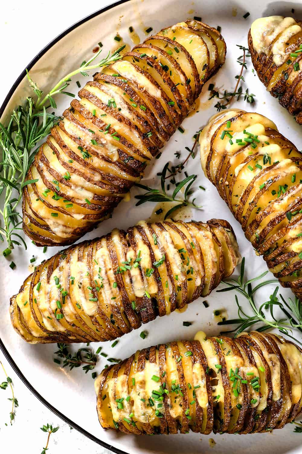top view of Hasselback potato recipe on a plate garnished with thyme and rosemary