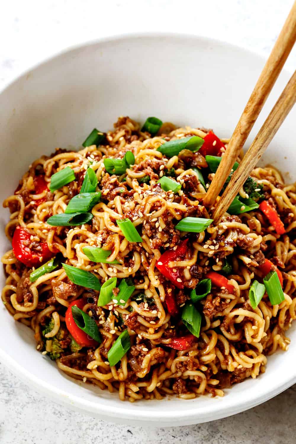 showing how to make ramen noodle stir fry by garnishing with sesame seeds and green onions