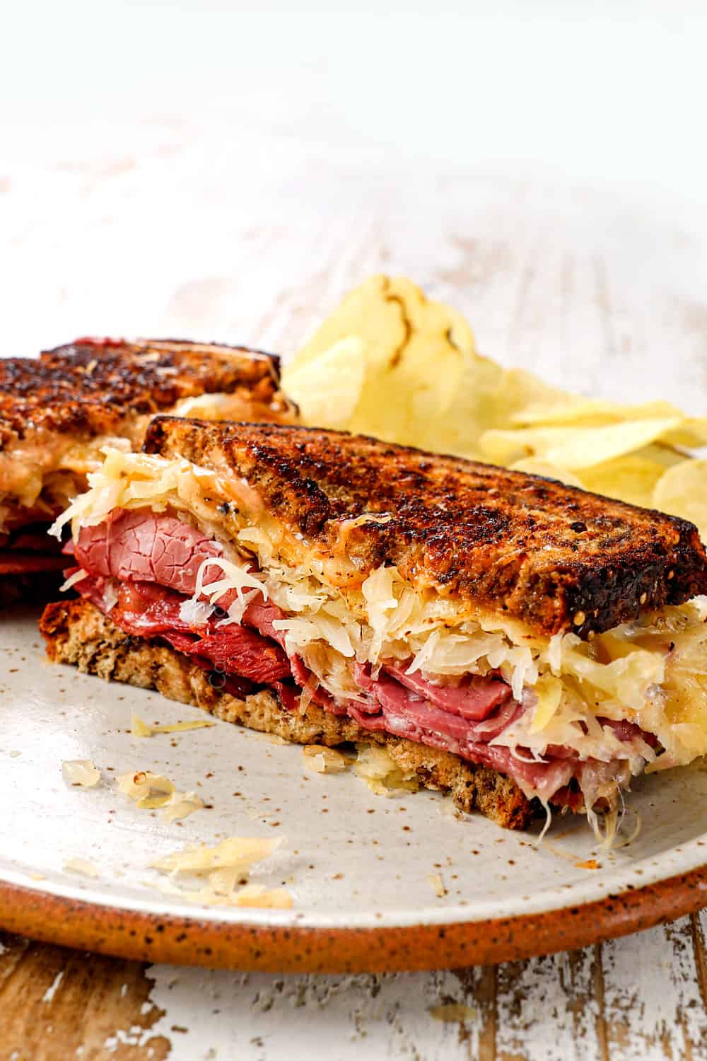 showing how to serve Rueben sandwiches with a Reuben sliced in half on a plate with potato chips